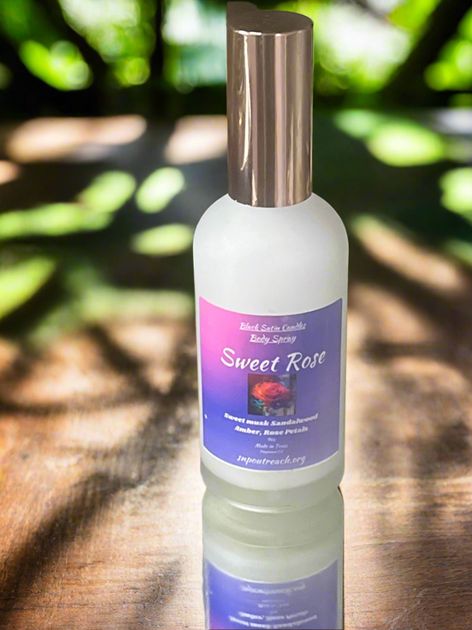 Bottle of 'Sweet Rose' body spray on a wooden surface with greenery in the background